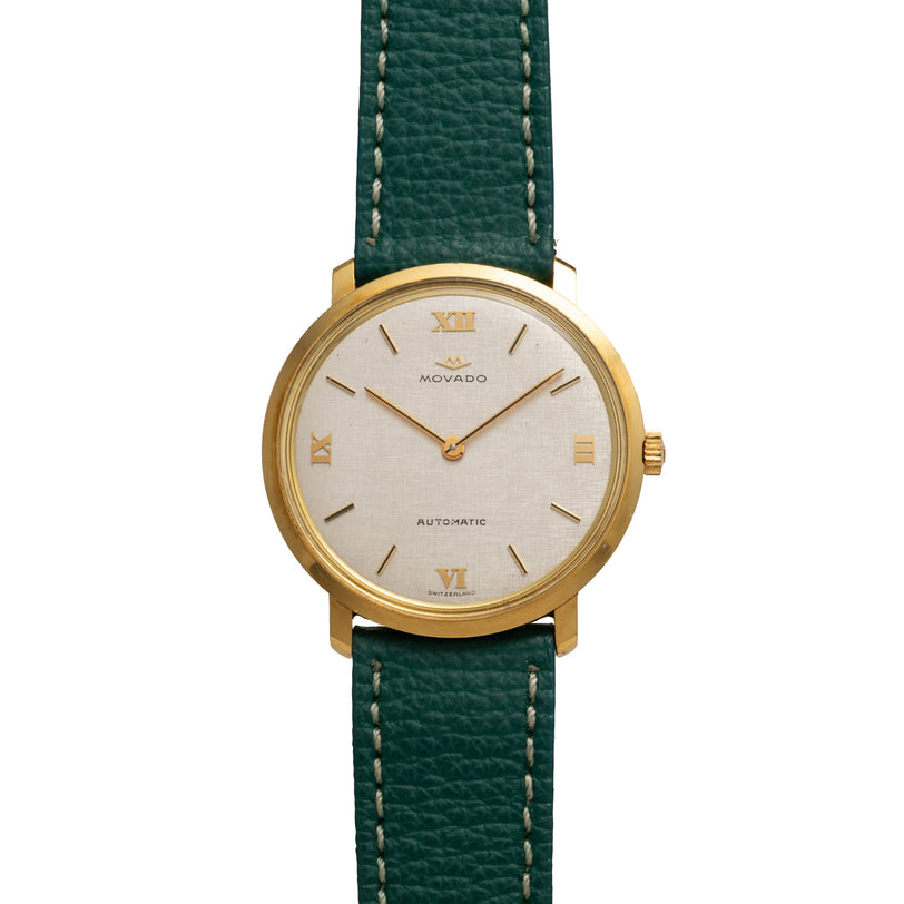 Movado watch with gold-tone case, cream dial, Roman numerals, and green leather strap with contrast stitching.