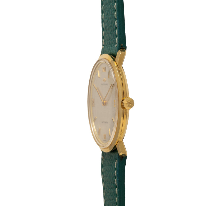 Gold-tone Movado watch with oval cream dial and Arabic numerals on green leather strap.