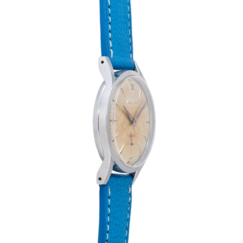 Movado watch with silver case, cream dial, and blue leather strap with white stitching.