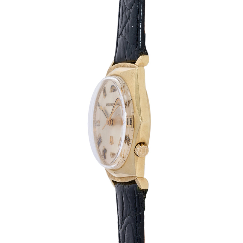 Bulova Accutron Delta Wing wristwatch with gold-tone case, cream dial, Arabic numerals, and black leather strap.