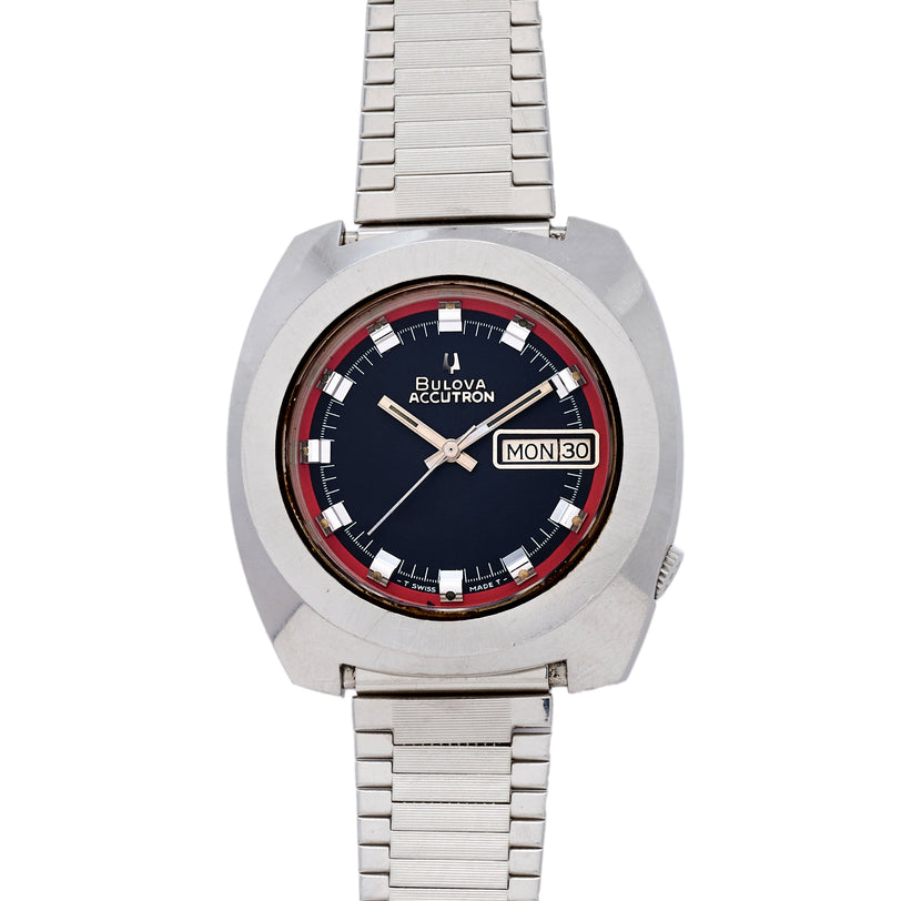 Bulova Accutron 218 stainless steel watch with black dial, red inner bezel, day-date window, and metal bracelet.