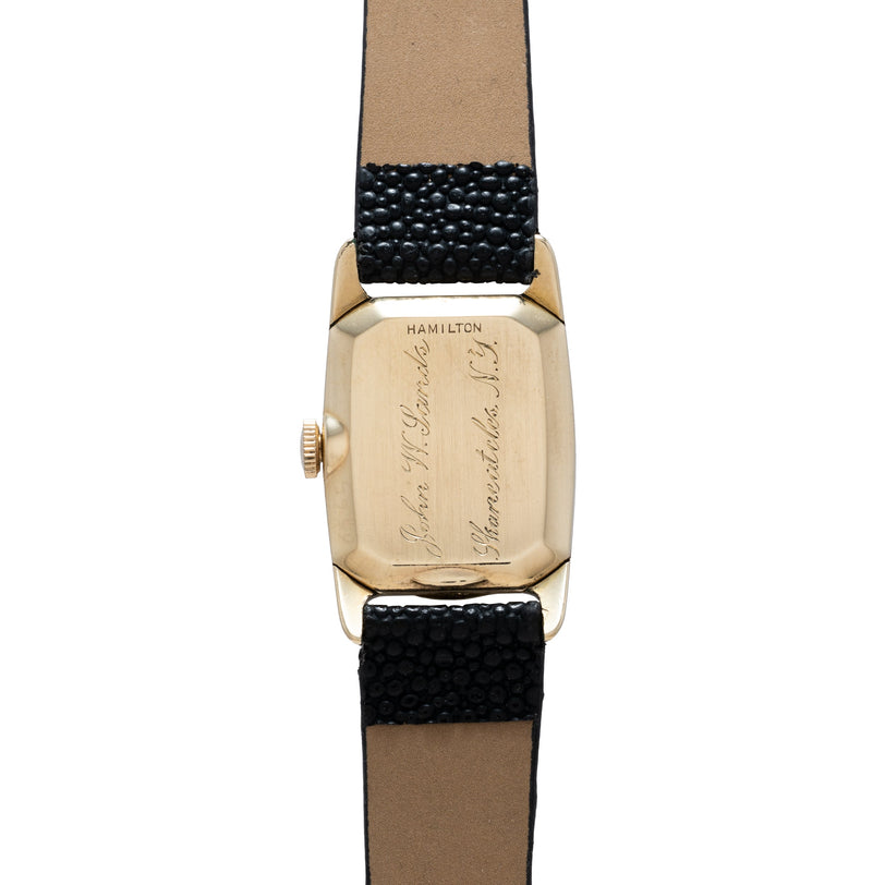 Hamilton Boulton watch with rectangular gold-tone case, engraved dial, black textured leather strap, and crown on side.