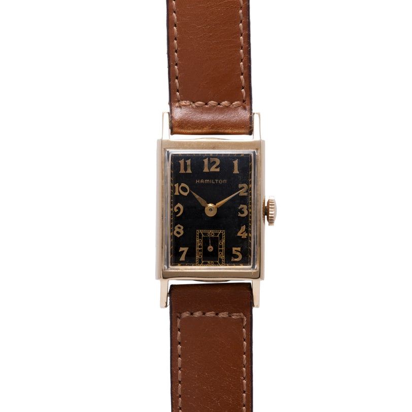 Hamilton Brock rectangular watch with black dial, gold numerals, and brown leather strap.