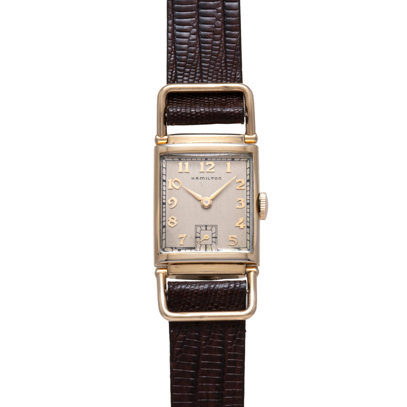 Hamilton rectangular watch with silver dial, gold numerals, and dark brown leather strap.