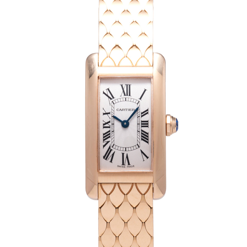 The Cartier Tank Americaine by Cartier is an 18K rose gold ladies' watch with a rectangular face, silver guilloché dial, black Roman numerals, blue sword hands, gold scale-pattern bracelet, and a crown set with a blue cabochon.
