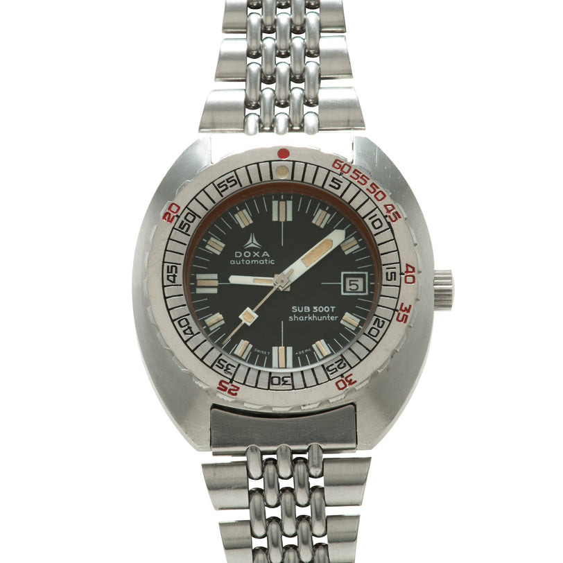 Stainless steel DOXA Sub 300T Sharkhunter watch with black dial, red bezel markings, and linked metal bracelet.