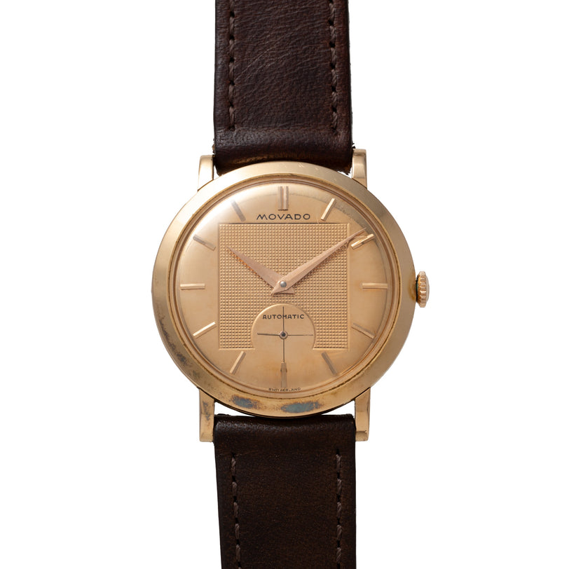 Movado Gentleman watch with gold-tone round case, textured dial, subdial, and dark brown leather strap.