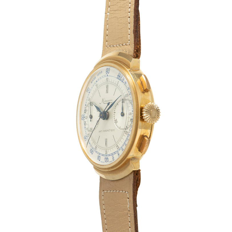 Gold chronograph watch with cream dial, blue hands, subsidiary dials, and tan leather strap with white stitching.