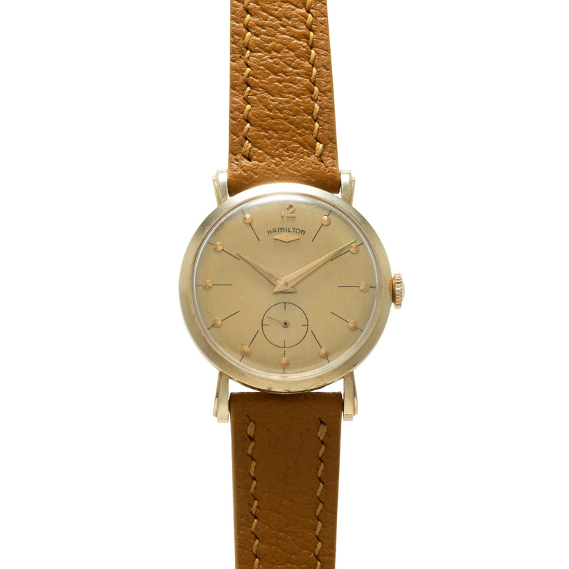 Hamilton watch with cream dial, gold-tone hands, and brown leather strap with white stitching.