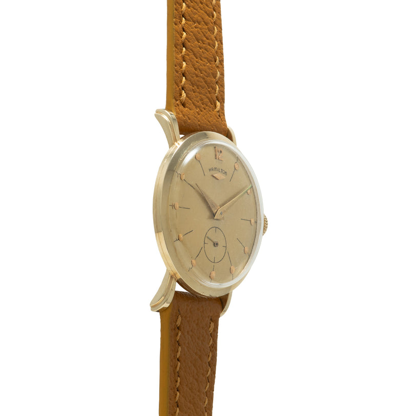 Hamilton wristwatch with oval silver-tone case, cream dial, and tan leather strap with white stitching.