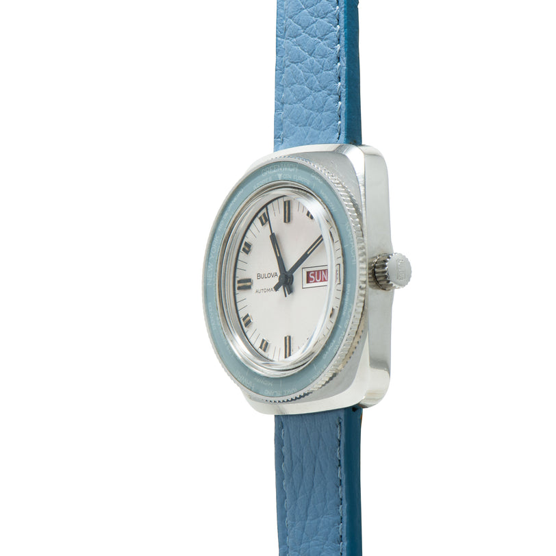 Bulova Skystar World Time watch with silver square case, light blue bezel, cream dial, day-date window, and blue leather stra