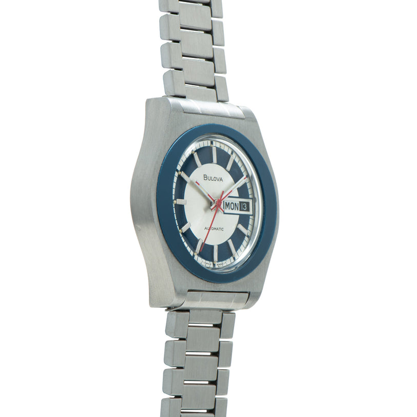 Bulova Jet Star watch with blue bezel, white dial, day-date window, and stainless steel bracelet.