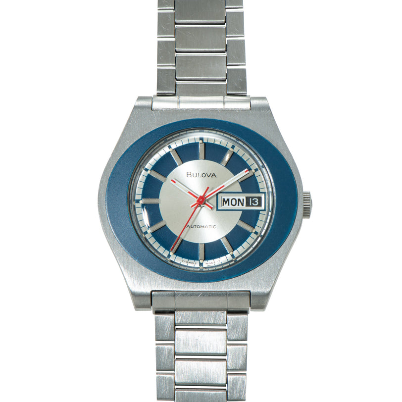 Bulova automatic watch with blue and silver dial, day-date window, red hands, and stainless steel bracelet.