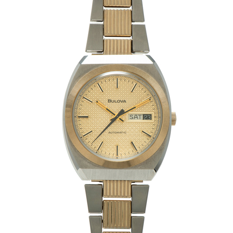 Bulova two-tone stainless steel and gold-toned watch with champagne dial, day-date window, and textured bracelet.