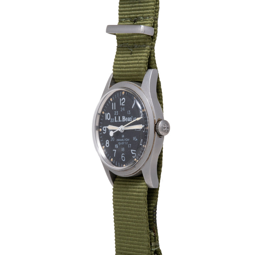 Hamilton Khaki Field watch with dark dial, silver hands, round stainless steel case, and olive green fabric strap.