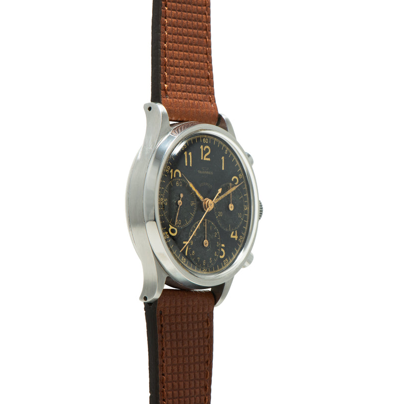 Vintage chronograph watch with dark dial, gold numerals and hands, stainless steel case, brown leather strap.