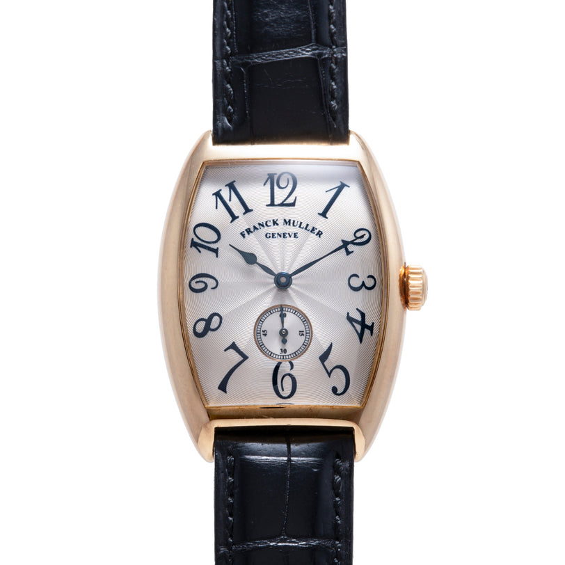 Gold-tone tonneau watch with silver dial, blue numerals, and black leather strap.