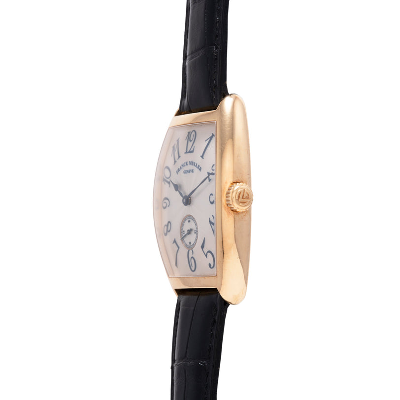 Gold-tone rectangular watch with curved case, cream dial, Arabic numerals, and black leather strap.