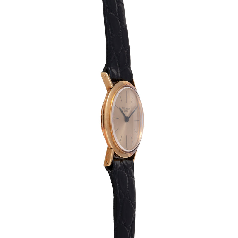 Rose gold oval watch with silver dial, applied indices, and black leather crocodile strap.