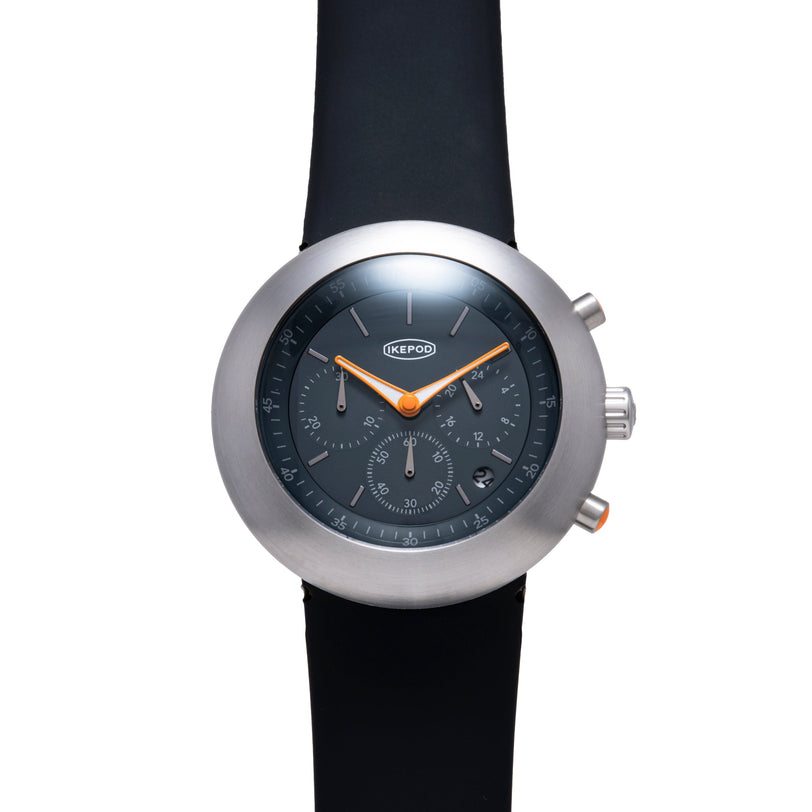Ikepod Chronopod watch with brushed steel case, dark dial, orange hands, and black rubber strap.