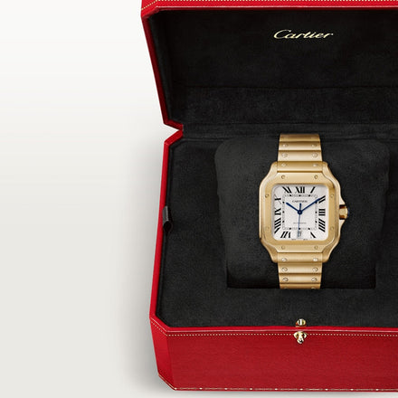 A gold Cartier watch sits on a black cushion in a red box