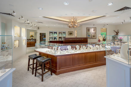 A bright jewelry store with glass display cases, wooden accents, and stools by the main counter.