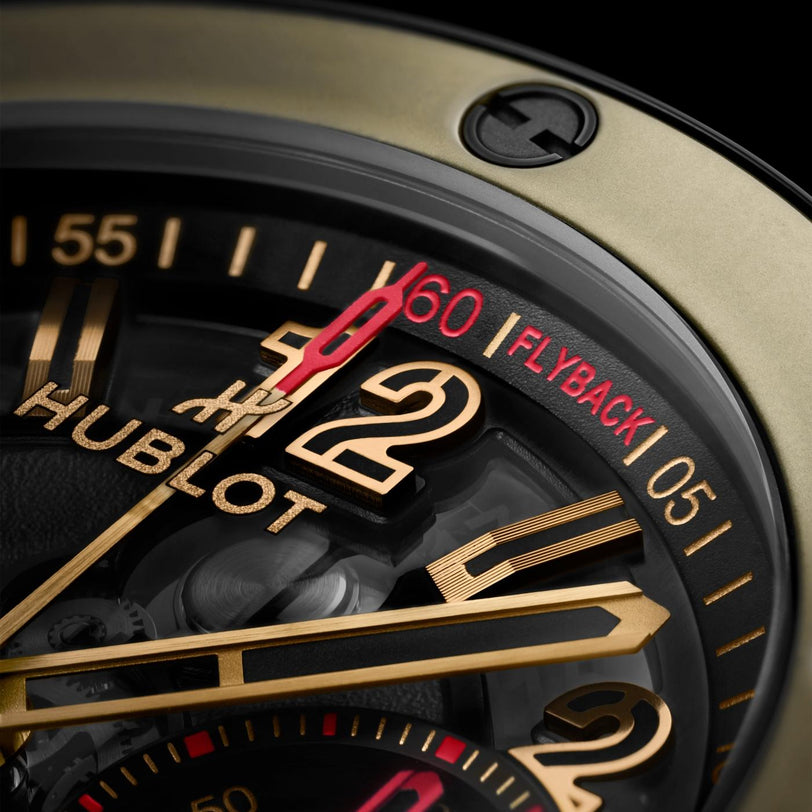 Watch face with gold and black dial, gold hands, red chronograph hand, and "60 FLYBACK" indicator on black bezel.