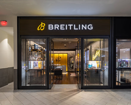 Breitling store with illuminated sign, glass entrance, and watch displays inside a shopping mall.