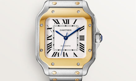 A close up view of the Santos de Cartier watch with gold and silver tone case and black roman numerals on a white dial