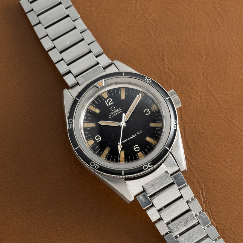 An OMEGA Seamaster 300 watch with a black dial and stainless steel bracelet rests on a brown surface.
