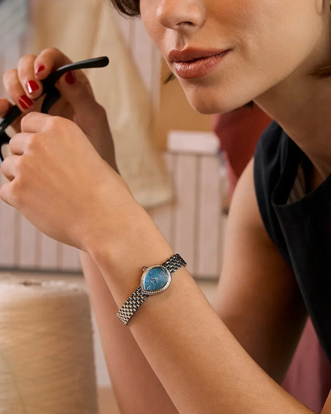 Light blue dial watch with stainless steel mesh band worn on woman's wrist.