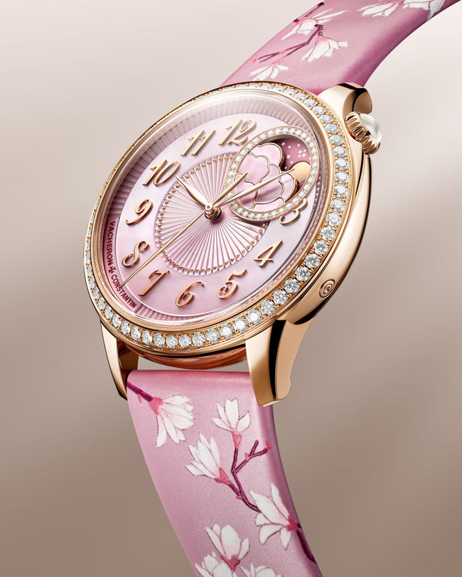 Rose gold watch with pink mother-of-pearl dial, crystal-set bezel, moon phase subdial, and pink silk strap with floral patter