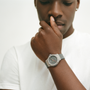 A person in a white t-shirt touches their face, wearing the Hublot Classic Fusion Titanium Limited Edition For Hodinkee wristwatch by Hublot, shown in close-up against a plain background.