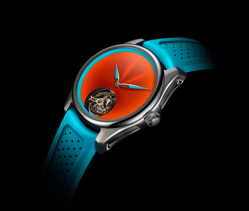 The H. Moser & Cie Pioneer Centre Seconds Spiced Aqua features a vibrant orange dial, visible tourbillon, and a blue perforated strap, displayed against a black background.
