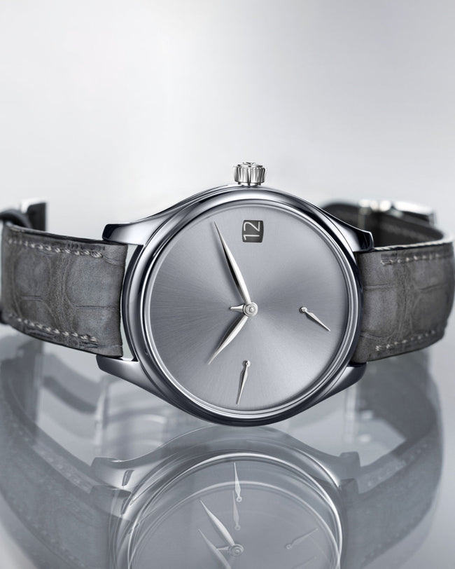 Tantalum watch with silver dial, minimalist hour markers, and dark leather strap displayed against reflective surface.