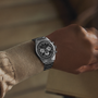 A person wearing a Zenith Chronomaster Original Triple Calendar Limited Edition For Hodinkee, featuring a silver case and black-and-white chronograph dial, dressed in a beige textured sweater and holding a light brown object.