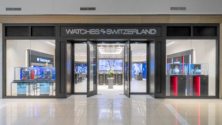 Front view of a Watches of Switzerland store with glass doors and luxury watch displays inside.