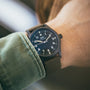 A person wearing an IWC Schaffhausen Pilots Watch Mark XVIII Edition HODINKEE with a black dial and nylon strap on their left wrist.