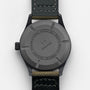 The image shows the back of a black IWC Schaffhausen Pilots Watch Mark XVIII Edition HODINKEE with a leather strap, engraved text around the case, and a central circular logo, highlighting its limited edition status.