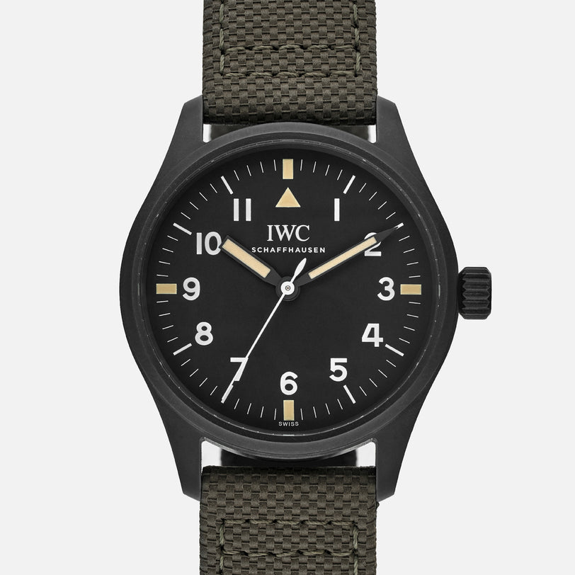 The IWC Schaffhausen Pilots Watch Mark XVIII Edition HODINKEE features a black dial with white numerals, a green textured fabric strap, and is displayed on a plain white background.