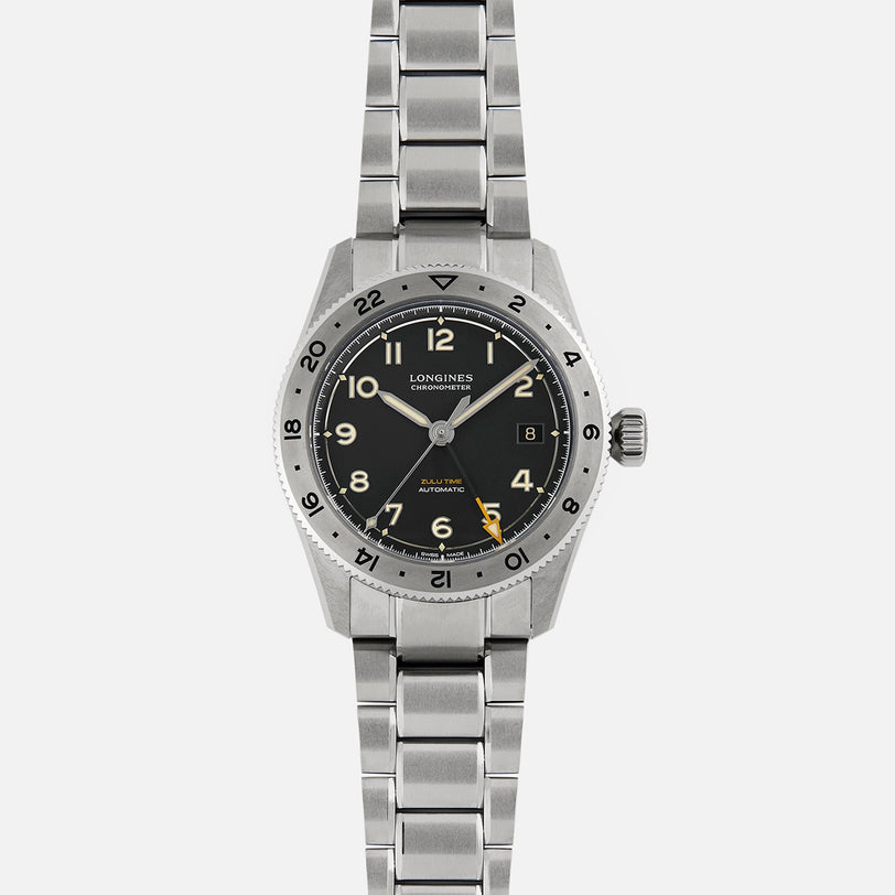 The Longines Spirit Zulu Time Limited Edition For Hodinkee features a black dial with Arabic numerals, date at 3 o’clock, and a metal bracelet. Crafted from Grade 5 Titanium by Longines, it is shown on a plain white background.