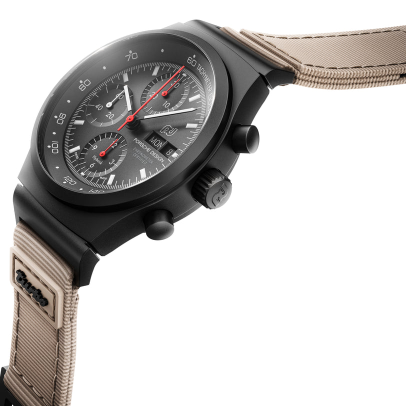The Porsche Design Chronograph 1 – 50 Years 911 Turbo Edition is displayed at an angle, featuring a black dial, red hands, and a beige strap.