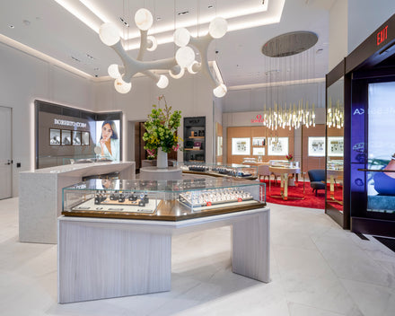 Modern jewelry store interior with glass display cases, bright lighting, and a floral arrangement on a counter.