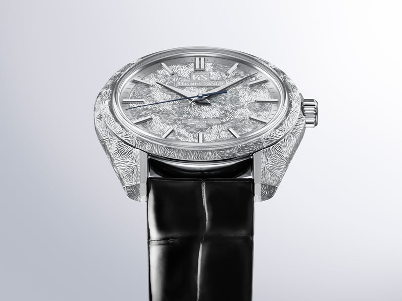 Silver watch with textured dial and case, black leather strap, round face with hour markers and hands.