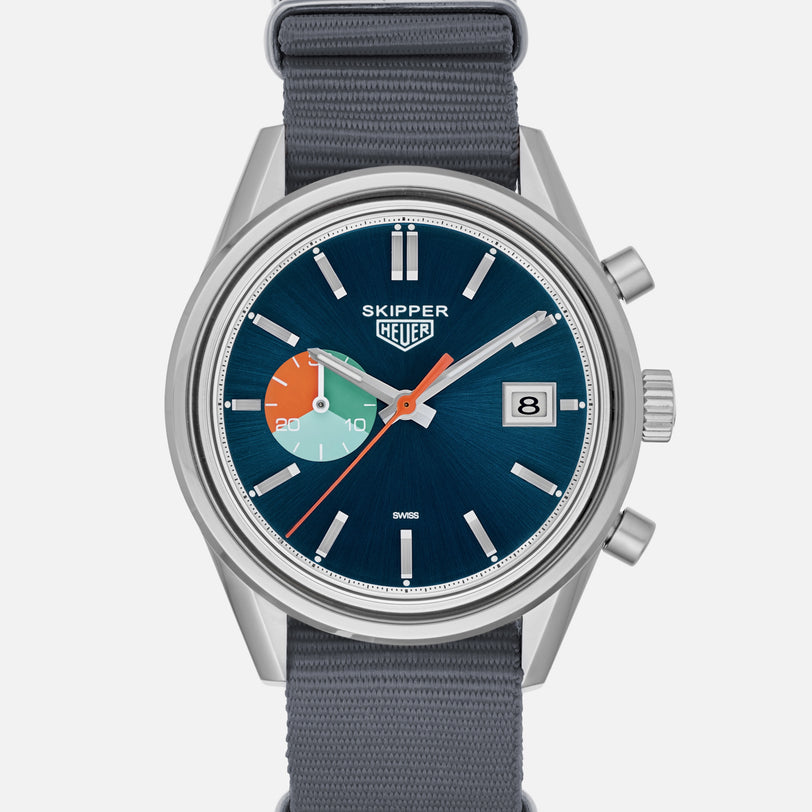 The TAG Heuer Limited Edition Carrera Skipper For HODINKEE features a blue dial, silver case, gray strap, three subdials (one multicolored), SKIPPER HEUER text, and a date window at 3 o’clock—ideal for vintage chronograph collectors.