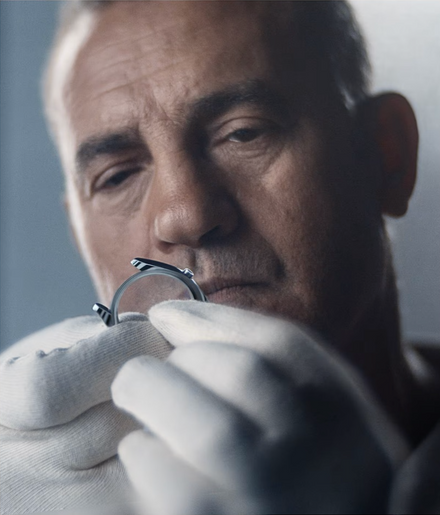 A man wearing white gloves closely examines a ring, focusing intently on its details.
