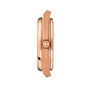 Side view of the Tissot PRX Powermatic 80 40mm rose gold wristwatch case with a crown displaying the T logo, set against a black background.
