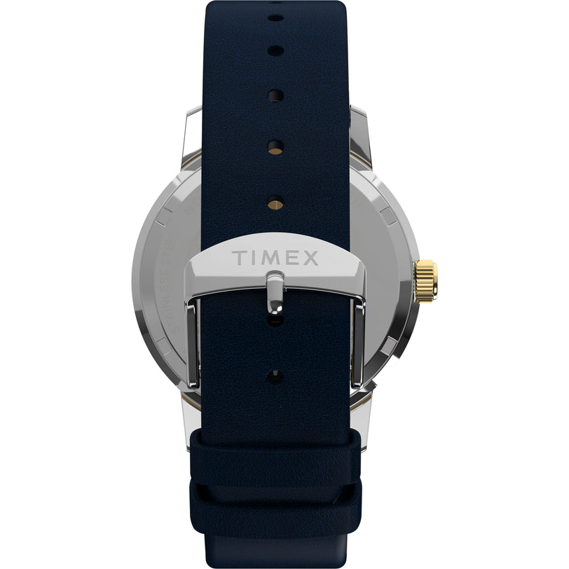 A close-up of the Timex Marlin® Quartz GMT wristwatch shows its navy blue leather strap, silver buckle engraved with TIMEX, gold-toned crown, and a vintage-inspired domed acrylic crystal on the case back.
