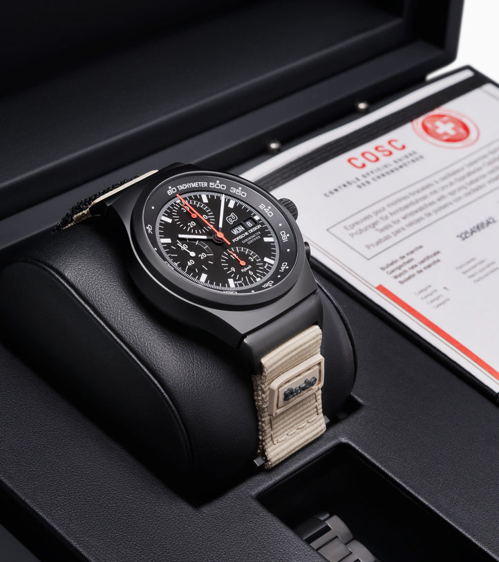 The Porsche Design Chronograph 1 50 Years 911 Turbo Edition features a black dial, beige strap, and comes in a display box alongside its COSC certification card.