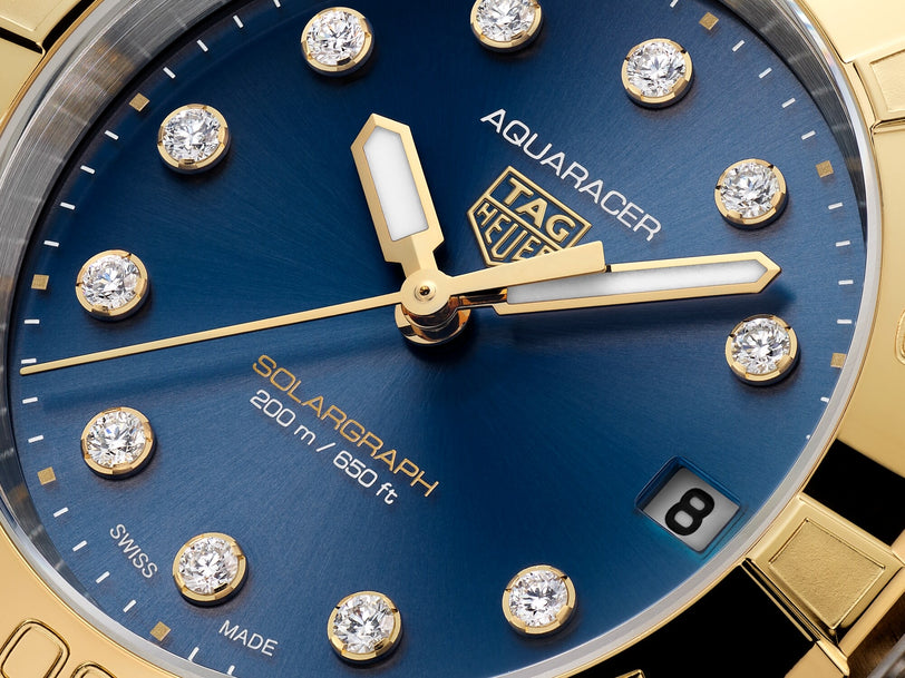 Close-up of a TAG Heuer Aquaracer Professional 200 Solargraph watch face in blue with gold accents and diamond hour markers.